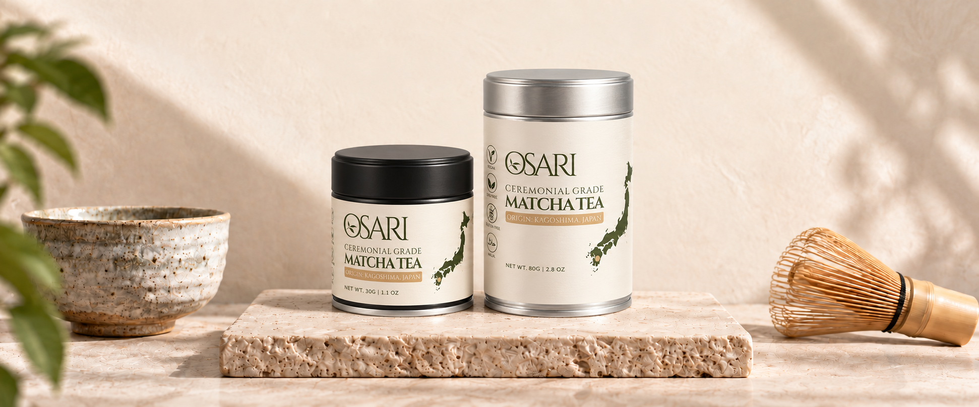 OSARI 30 g black-lid and 80 g silver-lid matcha tins with the original olive leaf-in-O mark, on a stone plinth beside a bowl and whisk